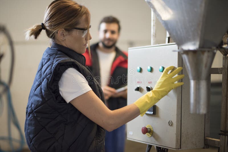 Mujer electricista en un panel de factoría, hombre de fondo imagenes de archivo