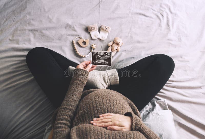 Mujer embarazada con imagen de ultrasonido lindo calcetines de bebé y juguetes en la cama en días de invierno fríos. mujer embaraz fotos de archivo