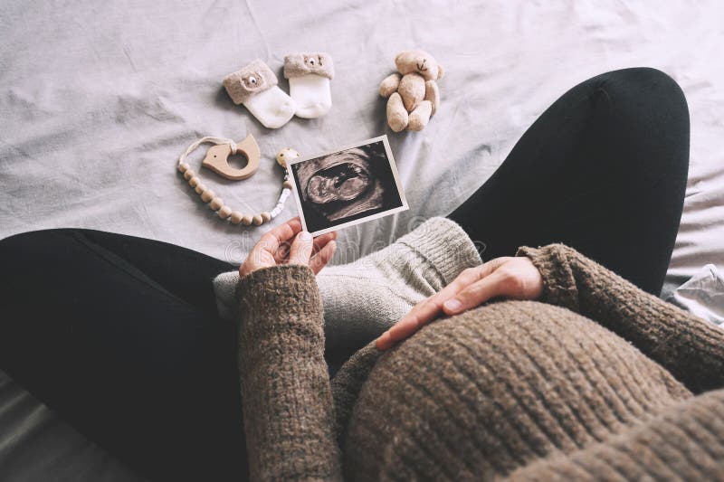 Mujer embarazada con imagen de ultrasonido lindo calcetines de bebé y juguetes en la cama en días de invierno fríos. mujer embaraz foto de archivo