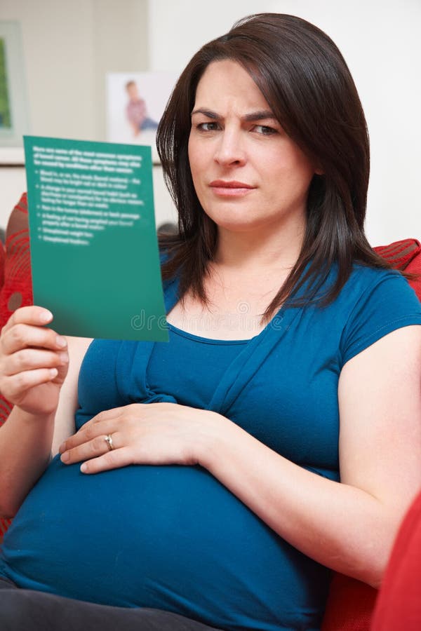 Mujer embarazada en cuestión que se sienta en Sofa Reading Leaflet fotos de archivo libres de regalías Mujer embarazada en cuestión que se sienta en Sofa Reading Leaflet fotos de archivo libres de regalías