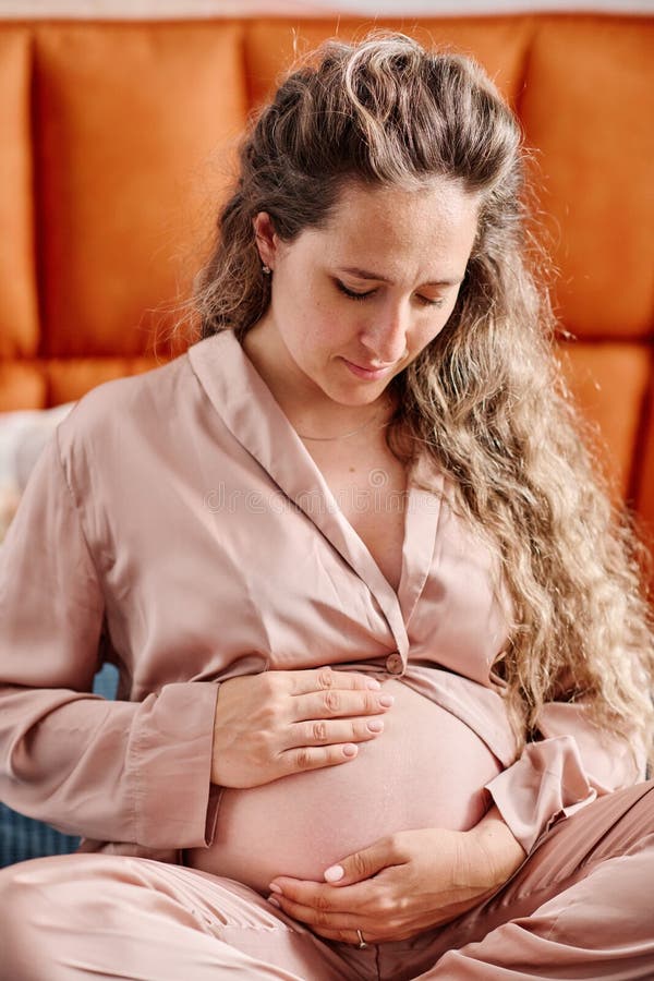 Mujer Embarazada En Pijama De Seda Mirando Su Vientre Y Tocándola Imagen de archivo Imagen de color, dormitorio: 252842463