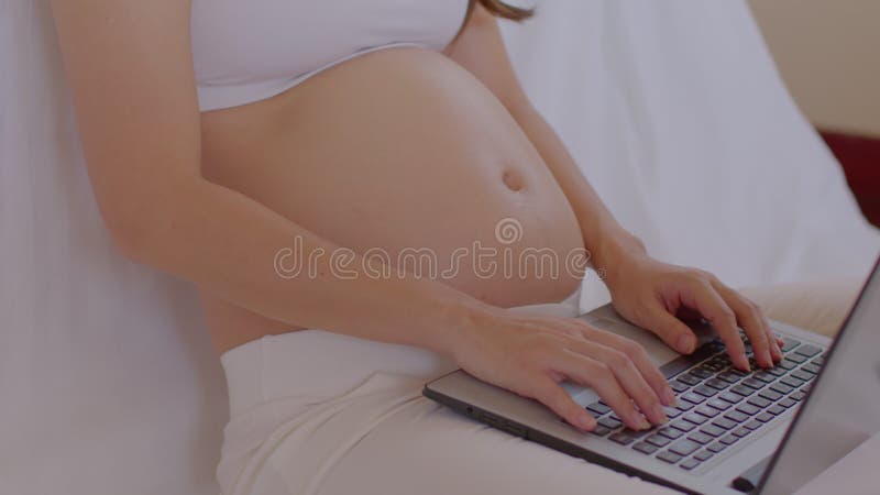 Mujer embarazada feliz sentada en la cama sosteniendo y acariciando su gran vientre en casa embarazo de una mujer joven disfrutand almacen de metraje de vídeo