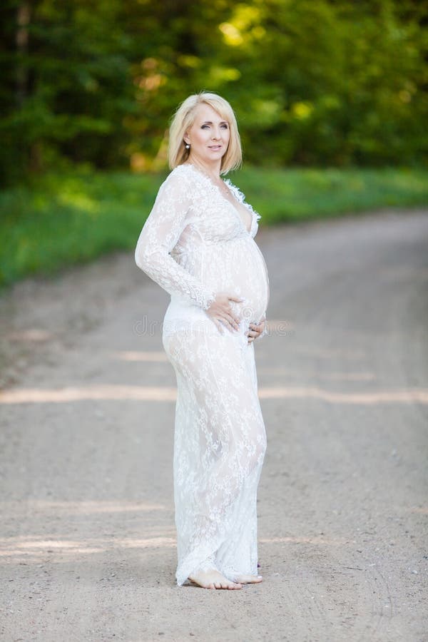 Mujer Embarazada Hermosa En El Vestido Maternidad Blanco De Encaje Largo Escarpado Que Parece Soñador En El Camino Solo En Bos Imagen de archivo - Imagen de hembra, muchacha: 131931489