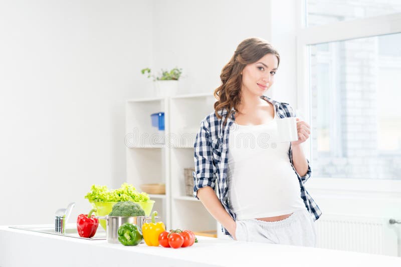 Mujer embarazada hermosa en la cocina con el panier y la manzana imagen de archivo Mujer embarazada hermosa en la cocina con el panier y la manzana imagen de archivo