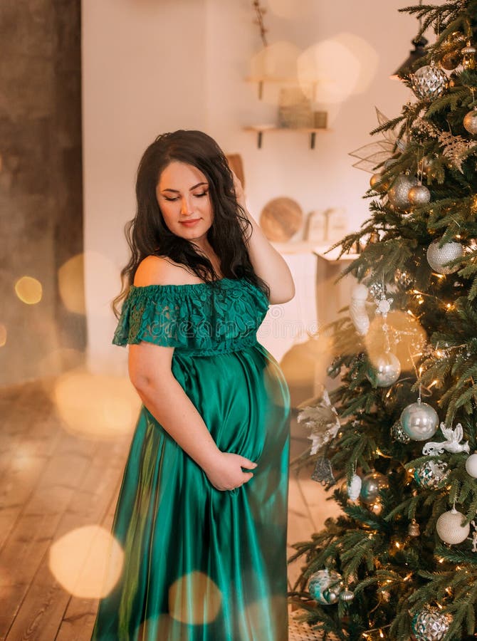 Mujer embarazada oscuro-cabelluda bonita en vestido largo esmeralda verde adorable magnífico cerca del árbol del Año Nuevo, señor imágenes de archivo libres de regalías Mujer embarazada oscuro-cabelluda bonita en vestido largo esmeralda verde adorable magnífico cerca del árbol del Año Nuevo, señor imágenes de archivo libres de regalías