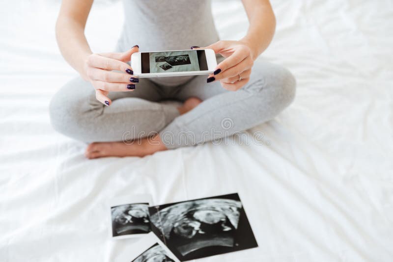 Mujer embarazada que toma imágenes de las fotos del ultrasonido con el teléfono celular imágenes de archivo libres de regalías Mujer embarazada que toma imágenes de las fotos del ultrasonido con el teléfono celular imágenes de archivo libres de regalías