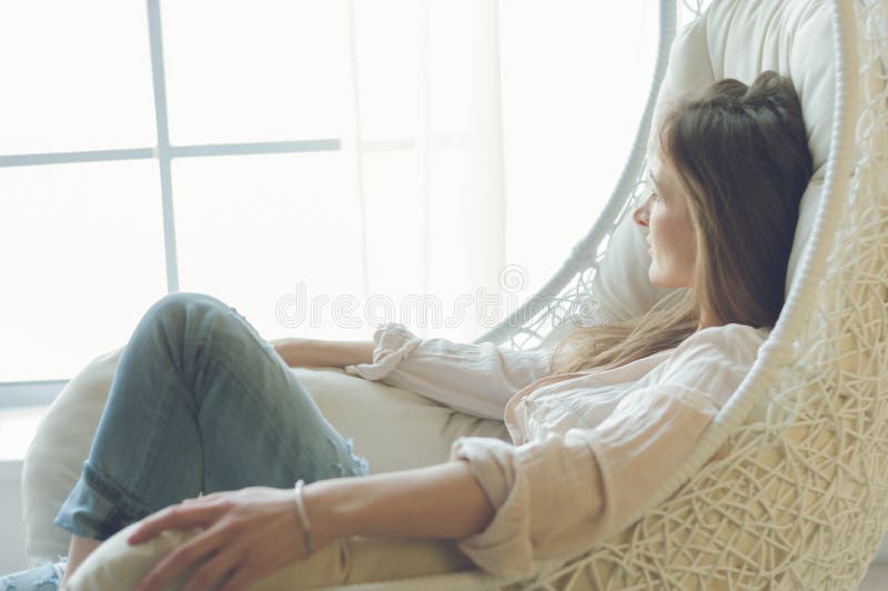 Mujer en casa que se sienta en silla moderna delante de la ventana que se relaja en su sala de estar fotografía de archivo Mujer en casa que se sienta en silla moderna delante de la ventana que se relaja en su sala de estar fotografía de archivo