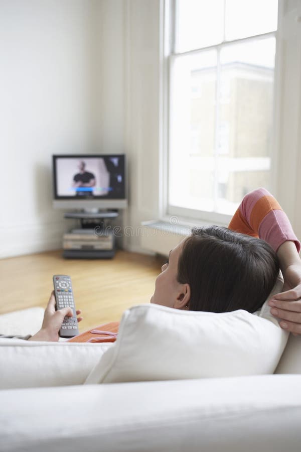 Mujer en el sofá que ve la TV imagen de archivo Mujer en el sofá que ve la TV imagen de archivo