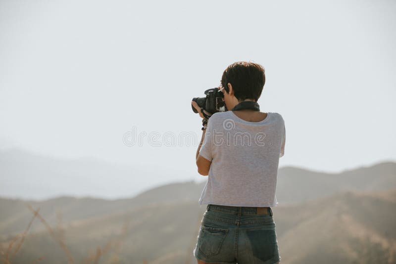 Mujer en la camiseta que toma una foto con una cámara del dslr en naturaleza con luz del día imágenes de archivo libres de regalías Mujer en la camiseta que toma una foto con una cámara del dslr en naturaleza con luz del día imágenes de archivo libres de regalías