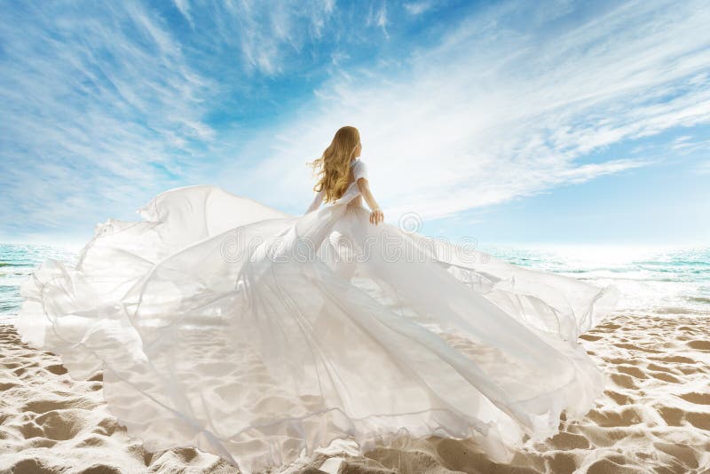 Mujer en la playa en vestido blanco volando en viento. vacaciones de verano. playa arena mar sol cielo