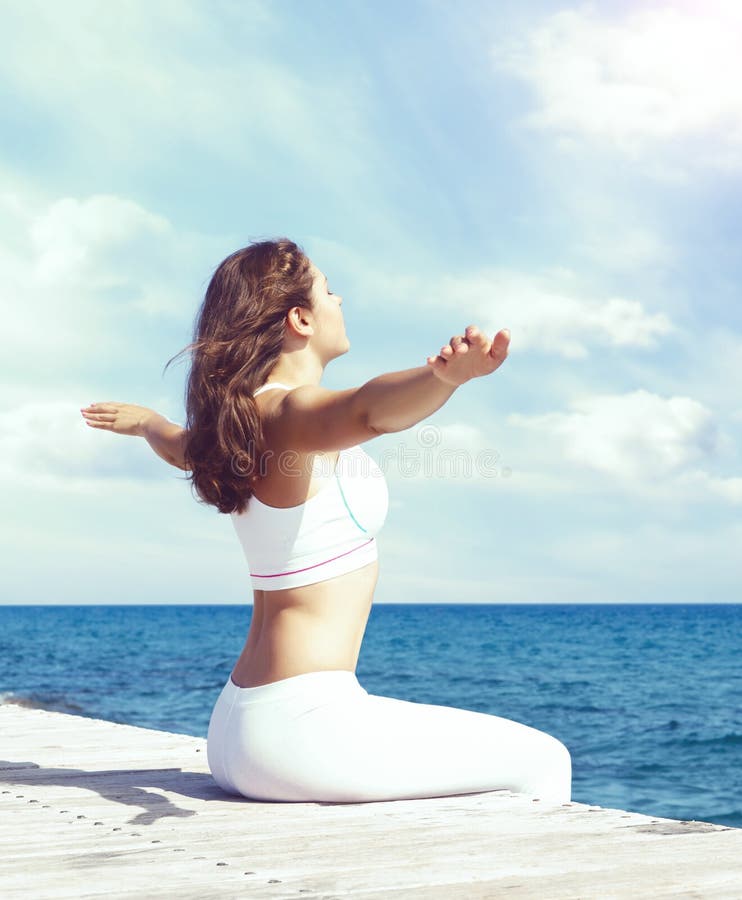 Mujer en la ropa de deportes blanca que hace yoga en un embarcadero de madera Mar y fotos de archivo Mujer en la ropa de deportes blanca que hace yoga en un embarcadero de madera Mar y fotos de archivo