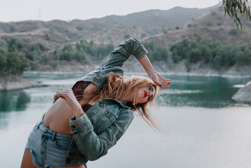 Mujer en pantalones cortos y chaqueta que presenta en naturaleza con un lago en el fondo imágenes de archivo libres de regalías Mujer en pantalones cortos y chaqueta que presenta en naturaleza con un lago en el fondo imágenes de archivo libres de regalías