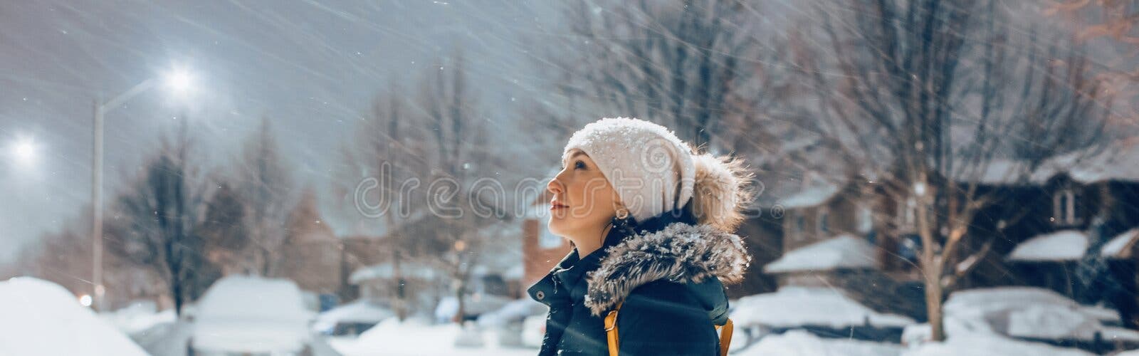 Mujer Con Ropa De Invierno Y Sombrero Caminando Al Aire Libre Bajo La Nieve.  Mujer De Pie Bajo La Luz De La Calle Mirando La Nieve Que Cae En La Noche.  País