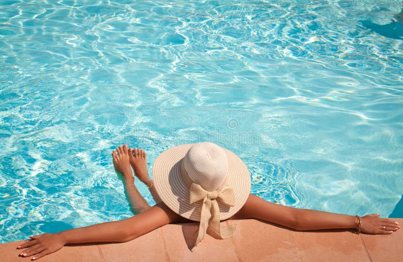 Mujer en un sombrero de la piscina que se relaja en una piscina azul fotos de archivo Mujer en un sombrero de la piscina que se relaja en una piscina azul fotos de archivo