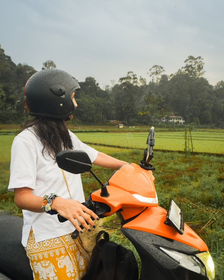 Mujer en una motocicleta en el campo de Sri Lanka sobre la lluvia mirando los exuberantes campos de arroz y colinas forestales en fotografía de archivo libre de regalías