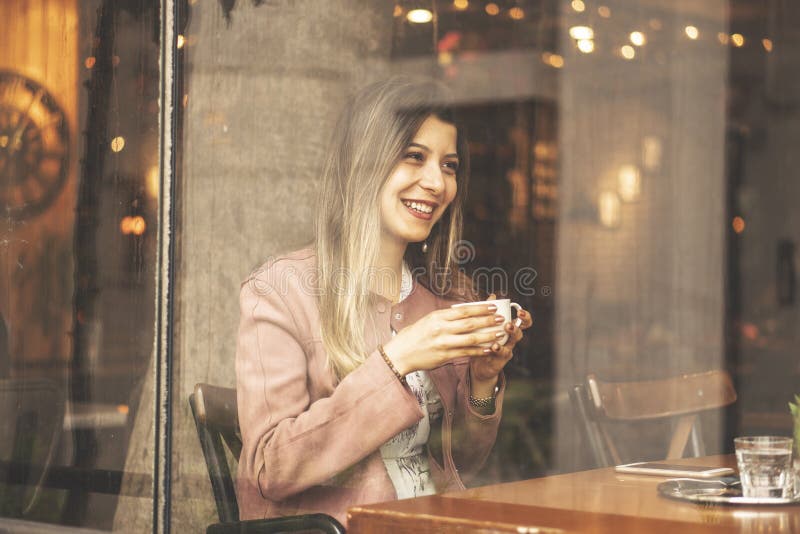 Mujer encantadora joven pasar tiempo mientras que se sienta en la cafetería durante tiempo libre, hembra atractiva con la sonrisa fotos de archivo libres de regalías Mujer encantadora joven pasar tiempo mientras que se sienta en la cafetería durante tiempo libre, hembra atractiva con la sonrisa fotos de archivo libres de regalías