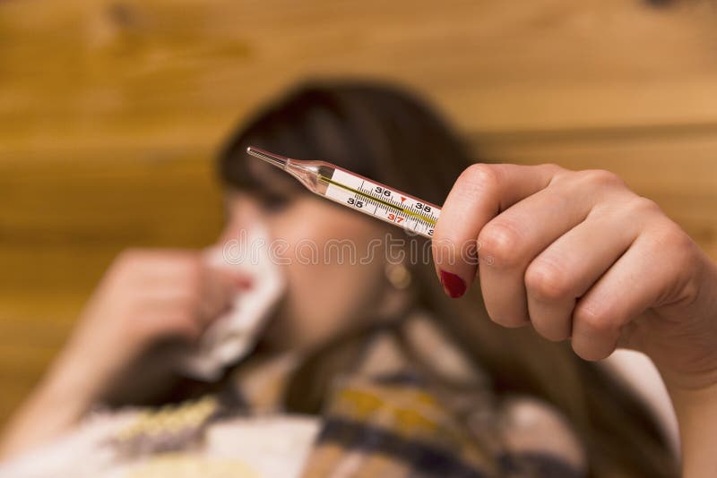 Mujer enferma en su cama que mira un termómetro clínico fotos de archivo libres de regalías Mujer enferma en su cama que mira un termómetro clínico fotos de archivo libres de regalías