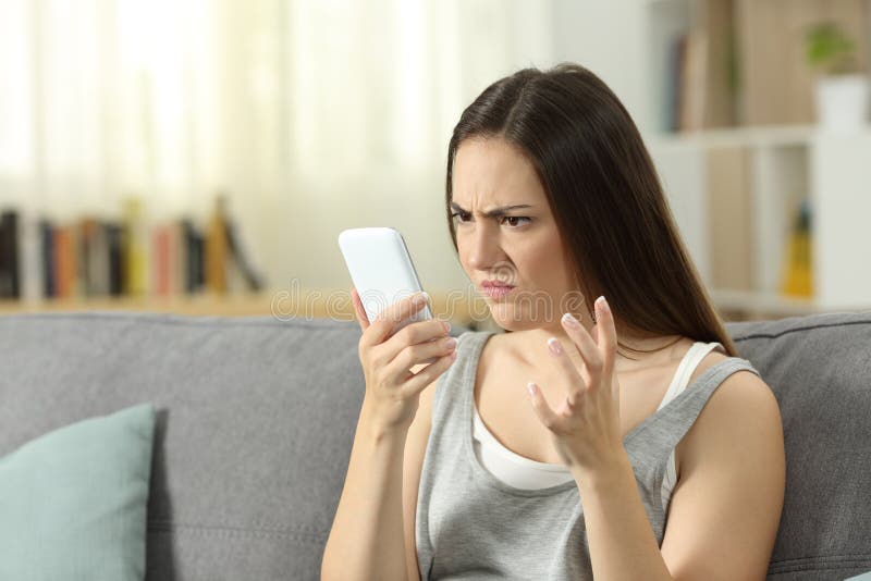 Mujer enojada que mira el teléfono elegante en casa fotografía de archivo Mujer enojada que mira el teléfono elegante en casa fotografía de archivo