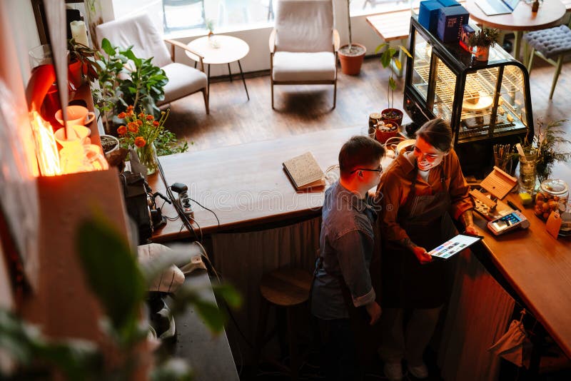 Mujer enseñando a un hombre con síndrome de baja para que use un comprimido durante la pasantía en el café fotografía de archivo libre de regalías