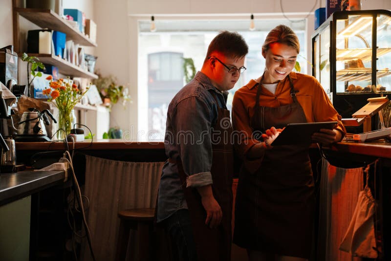 Mujer enseñando a un hombre con síndrome de Down cómo usar un comprimido durante la pasantía en el café fotos de archivo libres de regalías