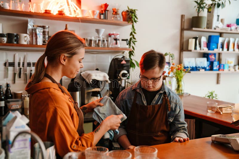 Mujer entrenando a un hombre con síndrome de Down para trabajar como barista en una cafetería imágenes de archivo libres de regalías