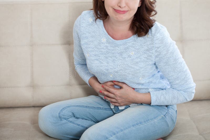 Mujer envejecida media que sufre de dolor abdominal mientras que se sienta encendido fotografía de archivo Mujer envejecida media que sufre de dolor abdominal mientras que se sienta encendido fotografía de archivo