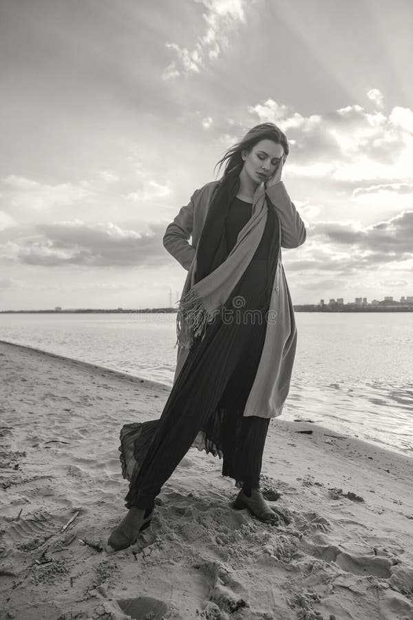 Mujer europea magnífica en capa y vestido calientes en un paseo en parque cerca del río Tiempo ventoso Su ropa vuela en el viento fotografía de archivo libre de regalías Mujer europea magnífica en capa y vestido calientes en un paseo en parque cerca del río Tiempo ventoso Su ropa vuela en el viento fotografía de archivo libre de regalías