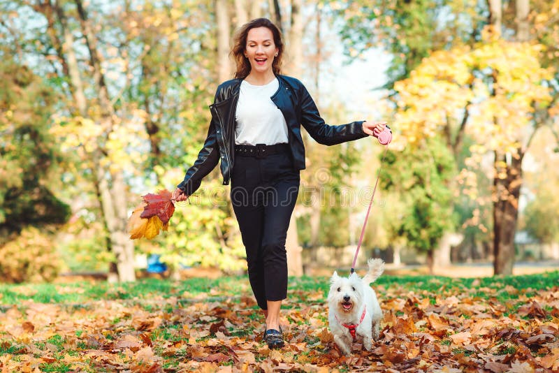 Mujer feliz corriendo con su pequeño territorio blanco de las tierras altas del oeste en un parque Chica elegante con perro camin fotografía de archivo Mujer feliz corriendo con su pequeño territorio blanco de las tierras altas del oeste en un parque Chica elegante con perro camin fotografía de archivo