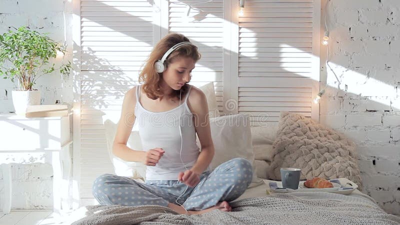 Mujer feliz en auriculares que escucha la música del smartphone y que baila en cama