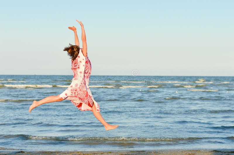 Mujer feliz joven que salta arriba en la playa fotografía de archivo Mujer feliz joven que salta arriba en la playa fotografía de archivo