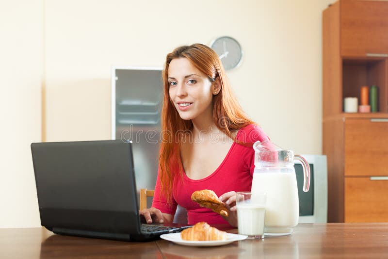 Mujer feliz joven que usa el ordenador portátil durante el desayuno en casa foto de archivo libre de regalías Mujer feliz joven que usa el ordenador portátil durante el desayuno en casa foto de archivo libre de regalías