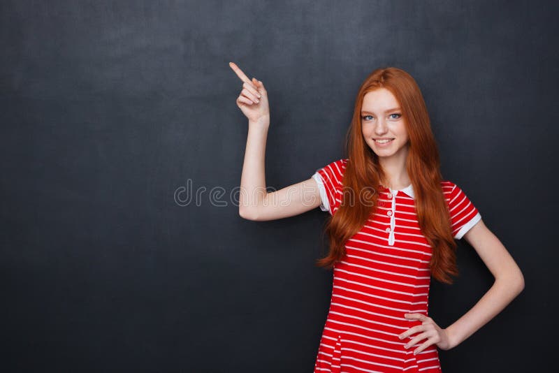 Mujer feliz linda que señala en copyspace sobre fondo de la pizarra foto de archivo libre de regalías Mujer feliz linda que señala en copyspace sobre fondo de la pizarra foto de archivo libre de regalías