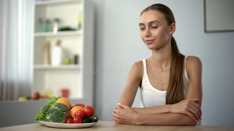 Mujer feliz que mira la placa con las verduras, nutrición sana, forma de vida del vegano fotografía de archivo libre de regalías Mujer feliz que mira la placa con las verduras, nutrición sana, forma de vida del vegano fotografía de archivo libre de regalías