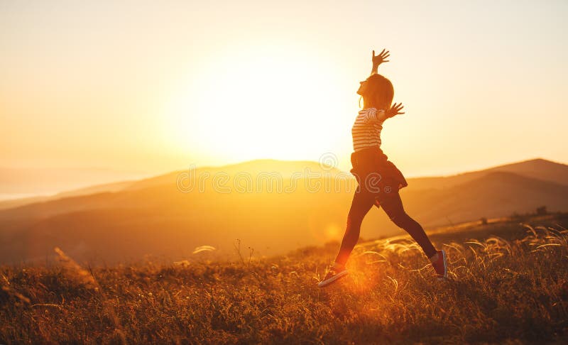 Mujer feliz que salta y que disfruta de vida en la puesta del sol en montañas fotografía de archivo libre de regalías