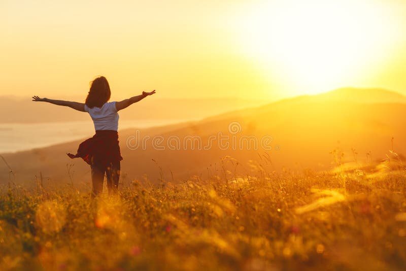 Mujer feliz que se coloca con ella detrás en puesta del sol en ope del iwith de la naturaleza