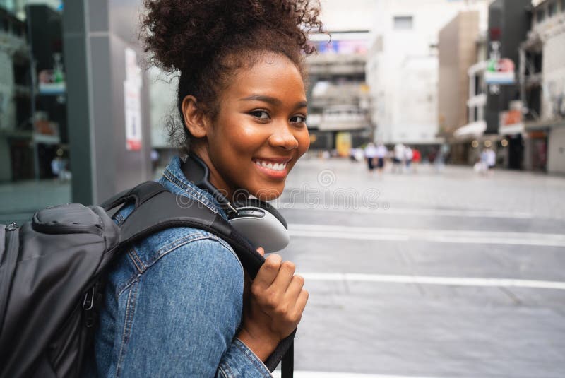 Mujer feliz sonriente caminando en la calle con mochila en la ciudad imagen de archivo