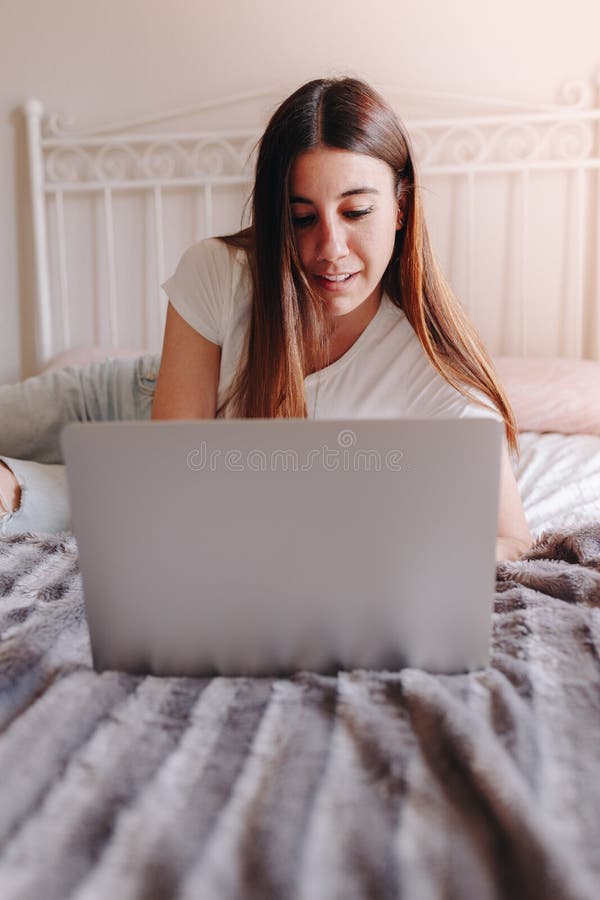 Mujer feminista joven hermosa que miente en la cama que sonríe y que escribe en el ordenador portátil fotos de archivo libres de regalías Mujer feminista joven hermosa que miente en la cama que sonríe y que escribe en el ordenador portátil fotos de archivo libres de regalías