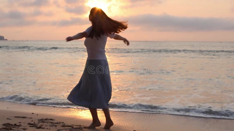 Mujer girando alegremente en la playa de la puesta del sol