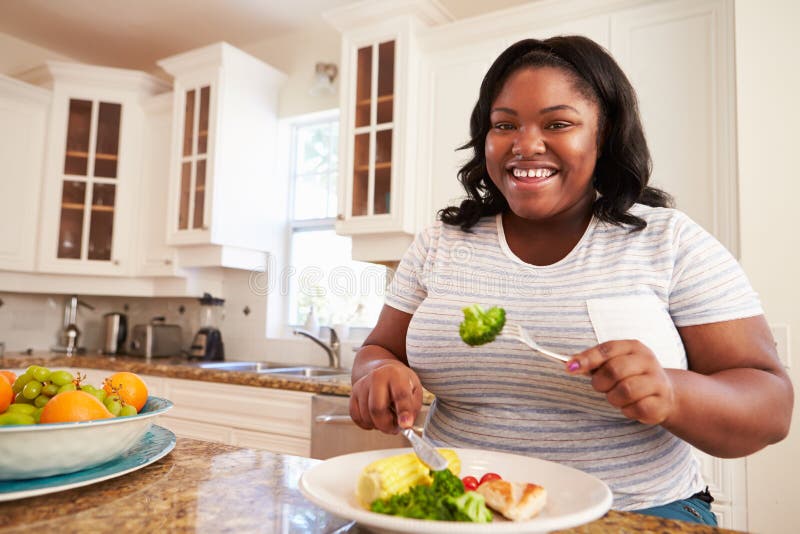 Mujer gorda que come la comida sana en cocina fotografía de archivo libre de regalías