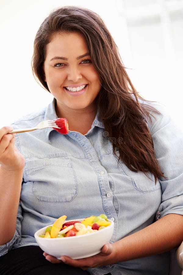 Mujer gorda que se sienta en la fruta de Sofa Eating Bowl Of Fresh imagen de archivo libre de regalías Mujer gorda que se sienta en la fruta de Sofa Eating Bowl Of Fresh imagen de archivo libre de regalías