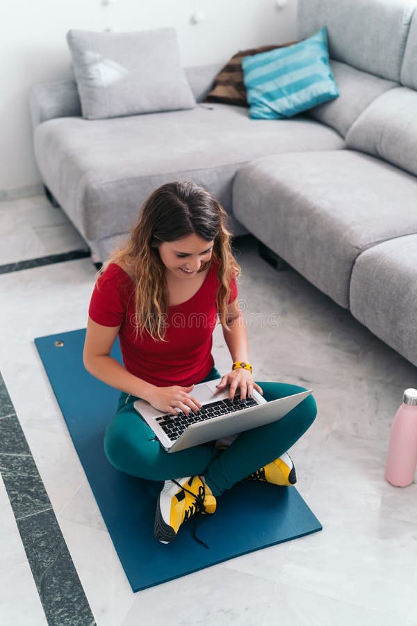 Mujer haciendo deportes en un tapete siguiendo clases en línea con laptop en casa imagenes de archivo