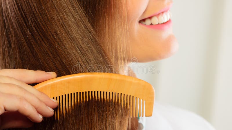 Health beauty and haircare concept - Closeup young business woman refreshing her hairstyle she combing her long brown hair with wooden comb. Health beauty and haircare concept - Closeup young business woman refreshing her hairstyle she combing her long brown hair with wooden comb