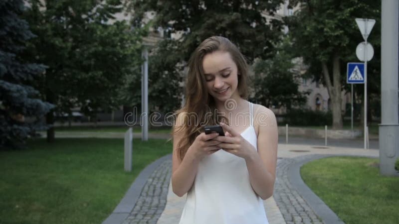 Mujer hermosa elegante que manda un SMS en smartphone en la ciudad