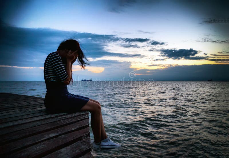 Beautiful woman in frustrated depression sitting on wooden bridge, near the beach on sunset. Concept of unemployed, sadness, depressed and human problems in dark tone. Beautiful woman in frustrated depression sitting on wooden bridge, near the beach on sunset. Concept of unemployed, sadness, depressed and human problems in dark tone.