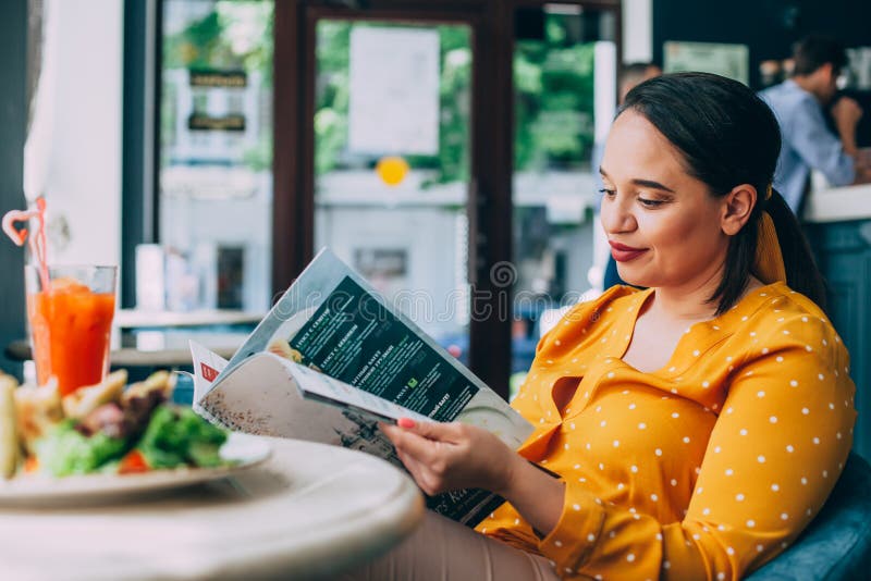 Mujer hermosa feliz del tamaño extra grande que come la ensalada y que bebe el smoothie sano en café imágenes de archivo libres de regalías Mujer hermosa feliz del tamaño extra grande que come la ensalada y que bebe el smoothie sano en café imágenes de archivo libres de regalías