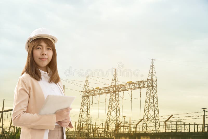 Mujer hermosa joven elegante del ingeniero eléctrico que trabaja usando la tableta para comprobar las redes eléctricas en la fábr foto de archivo Mujer hermosa joven elegante del ingeniero eléctrico que trabaja usando la tableta para comprobar las redes eléctricas en la fábr foto de archivo