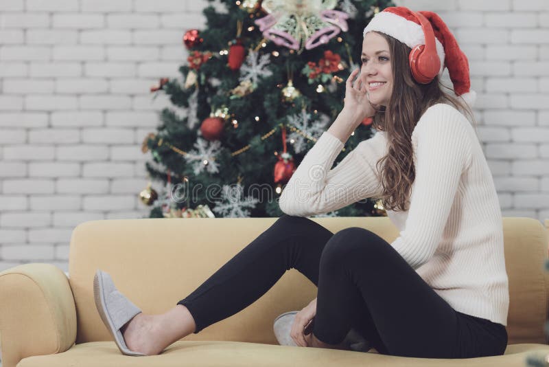 Mujer hermosa joven en el sombrero rojo que se sienta en el sofá entre el christm imágenes de archivo libres de regalías Mujer hermosa joven en el sombrero rojo que se sienta en el sofá entre el christm imágenes de archivo libres de regalías