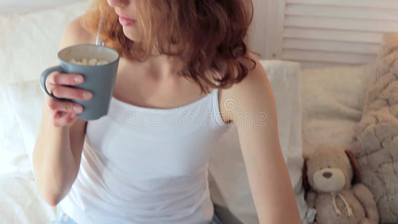 Mujer hermosa joven que come el desayuno en cama y que bebe el café