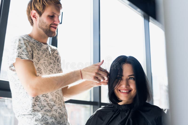 Mujer hermosa joven que hace su pelo cortar en el ` s del peluquero Peluquero de sexo masculino joven que sonríe y que hace el pe fotos de archivo Mujer hermosa joven que hace su pelo cortar en el ` s del peluquero Peluquero de sexo masculino joven que sonríe y que hace el pe fotos de archivo