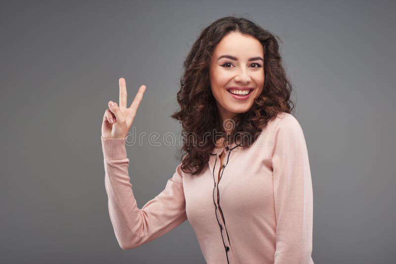 Mujer hermosa que sonríe y que muestra la muestra de la victoria foto de archivo Mujer hermosa que sonríe y que muestra la muestra de la victoria foto de archivo